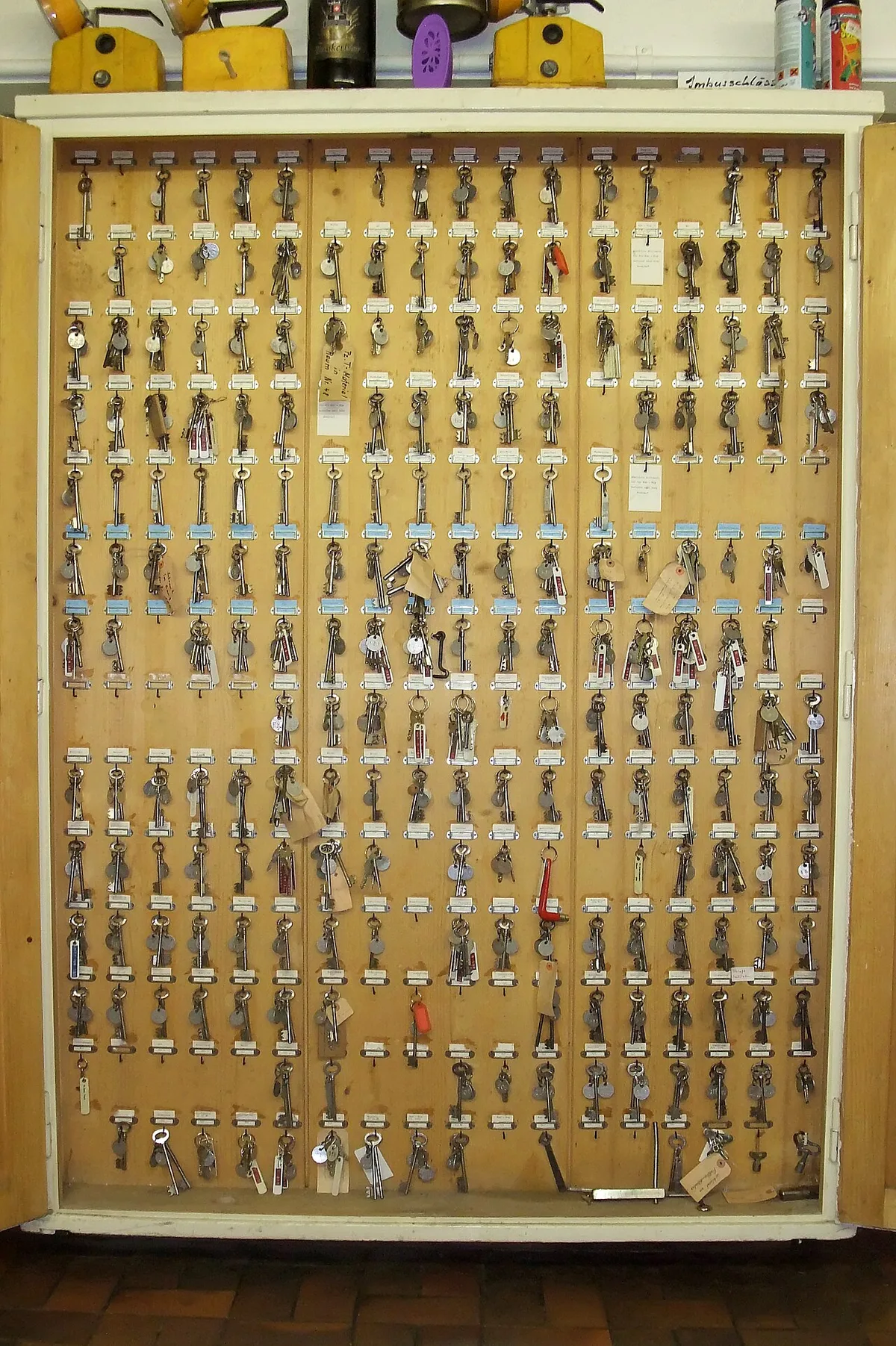 Een groot houten sleutelbord met tientallen rijen genummerde haakjes waaraan sleutelbossen met labels hangen.