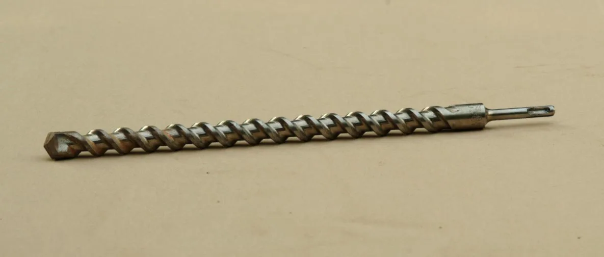 De punt van een steenboor met een hardmetalen snijplaatje, van dichtbij gefotografeerd tegen een donkere achtergrond.
