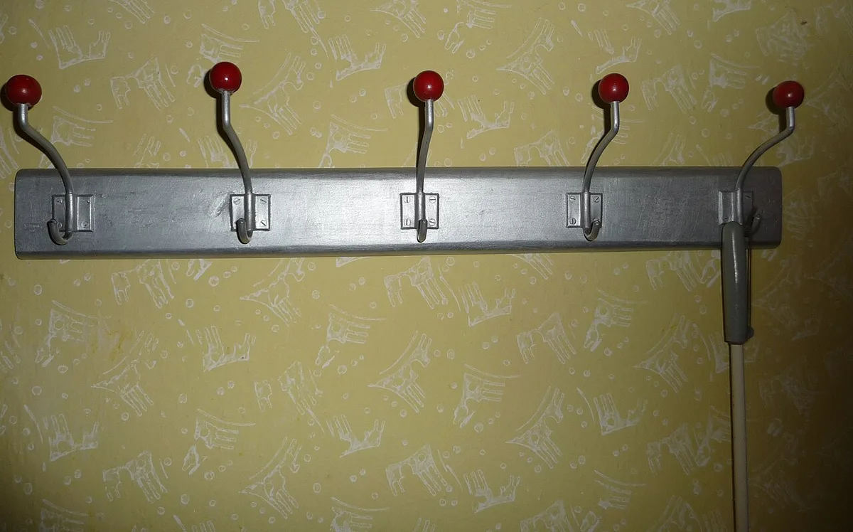 Een metalen kapstoklat met vier haken met rode knoppen, gemonteerd op een muur met okergeel behang.