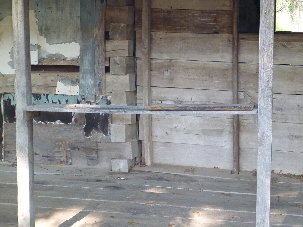 Een eenvoudige houten plank als wandplankje bevestigd aan de gevel van een houten hut.